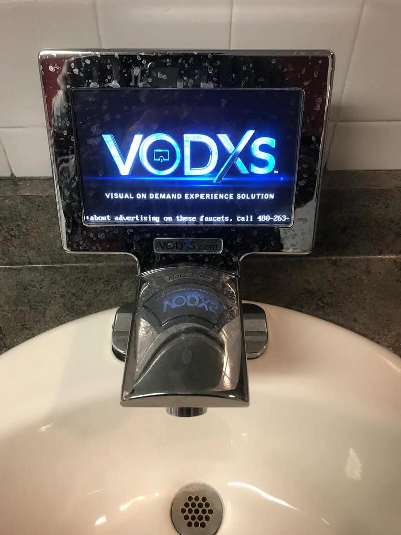 VODXS digital advertising display above a sink with water droplets on it.