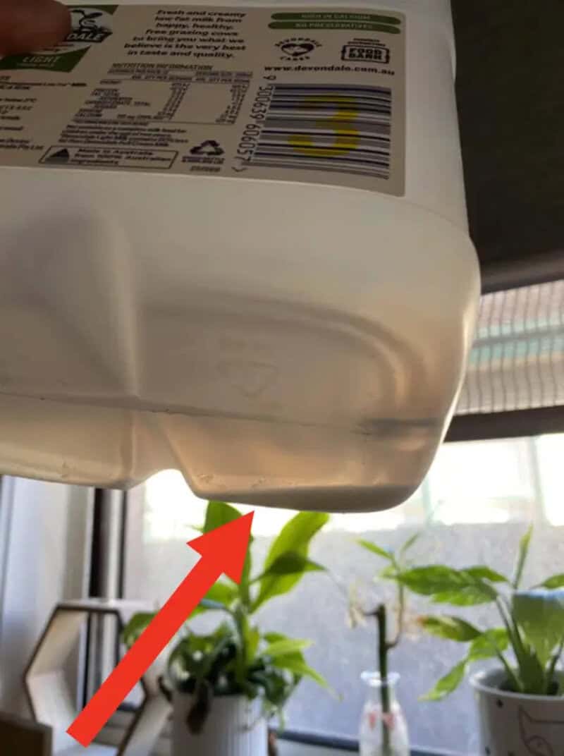 Close-up of a milk carton with a red arrow pointing to a small tear.