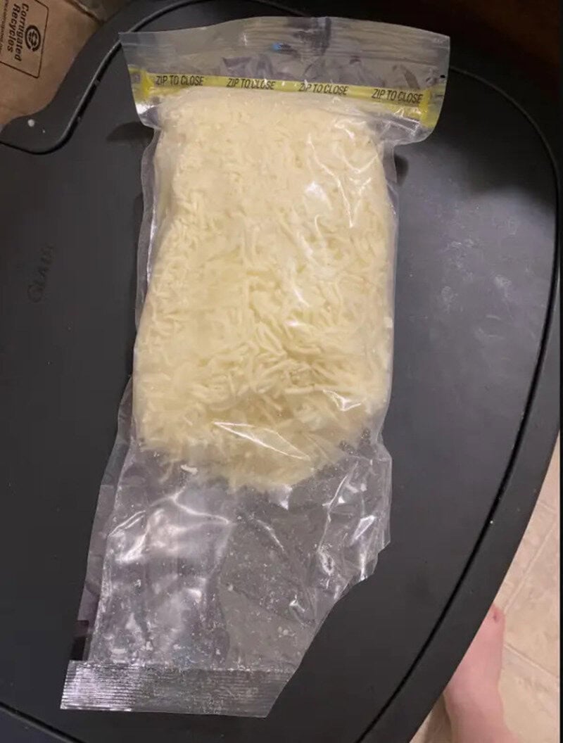 Frozen shredded cheese in a clear plastic bag on a black surface.