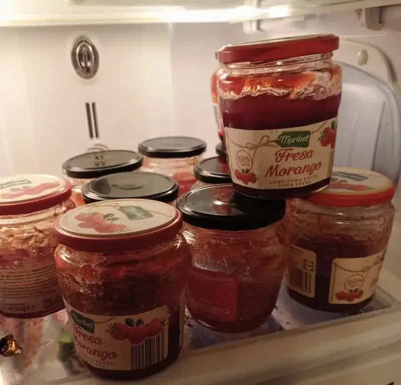 Multiple jars of strawberry jam inside a refrigerator, some stacked and some standing.
