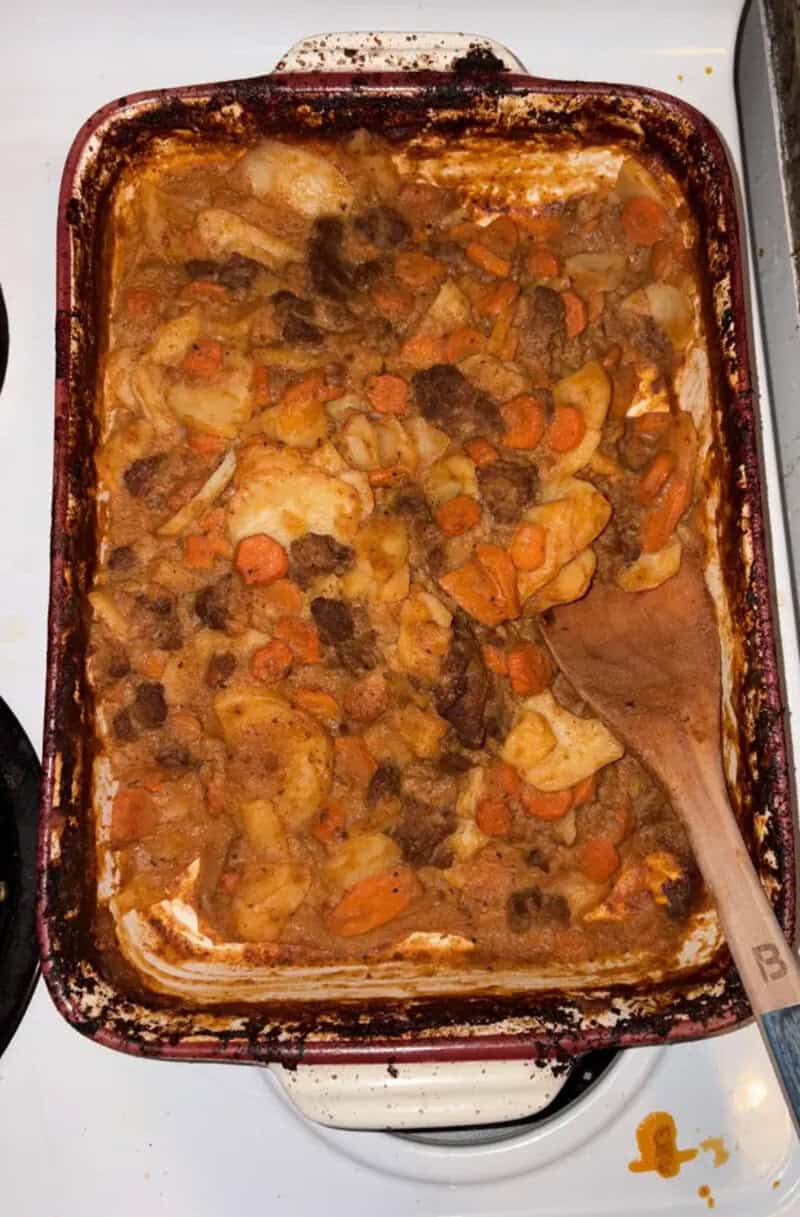 A baked casserole with meat, carrots, and potatoes in a glass dish.