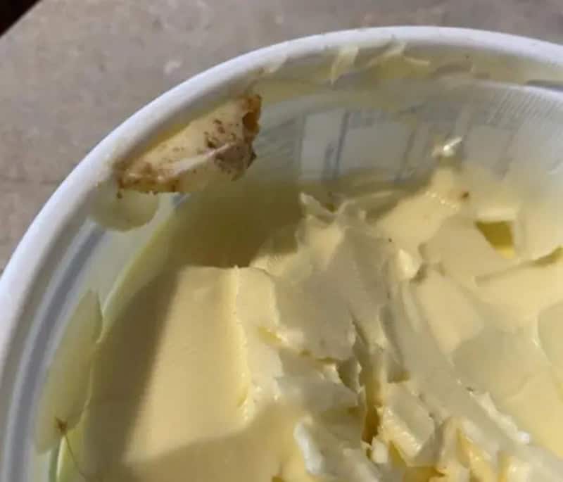 Close-up of a partially eaten tub of butter with a piece missing from the lid.