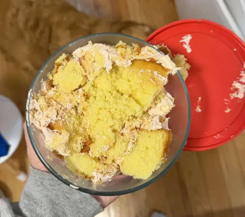 Frozen yellow cake with frosting in a glass, red lid nearby, wooden floor background.