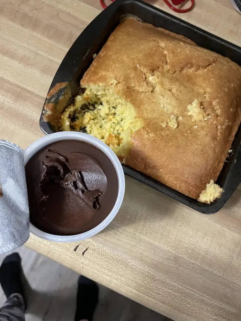 A large baked dish with a portion missing, next to a cup of chocolate pudding.