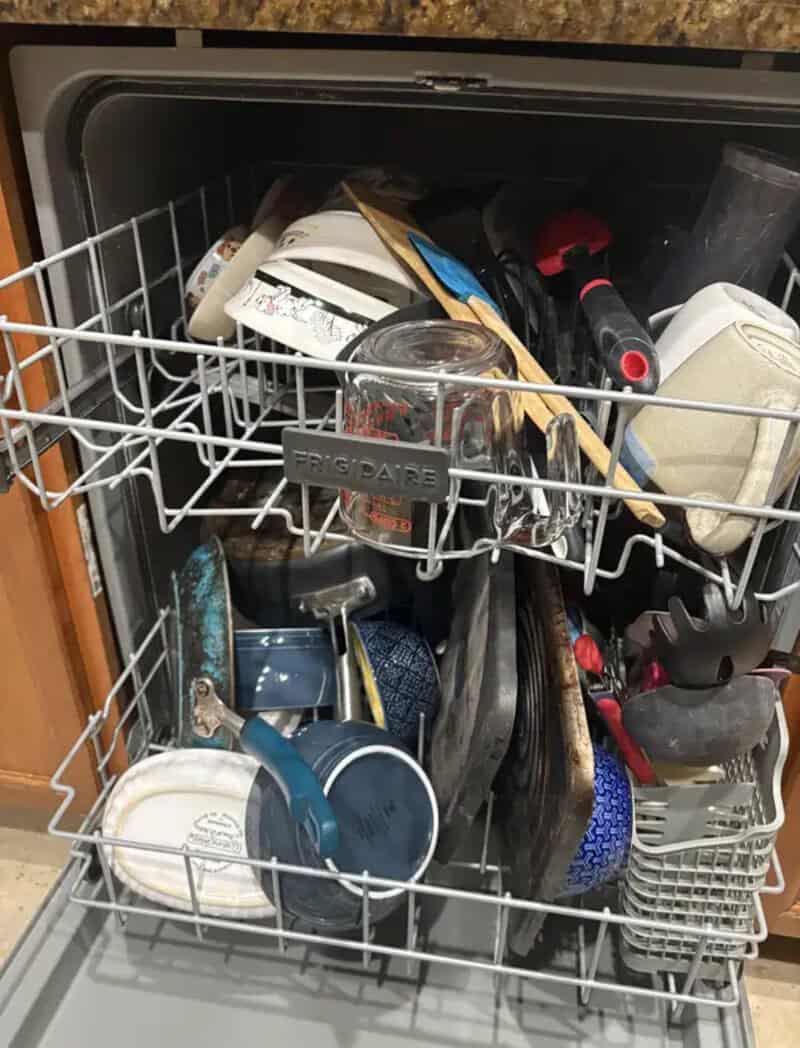 Cluttered dishwasher with dishes, utensils, and kitchen tools.