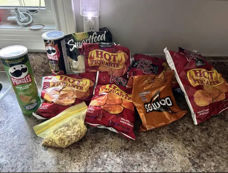 Assorted snacks on a kitchen counter, including Pringles, Hot Piquante chips, and a snack bag.