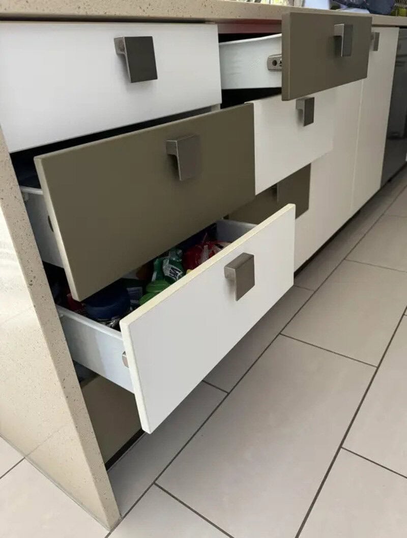 Drawers in a kitchen cabinet, some open and some closed, with a mix of white and gray colors.