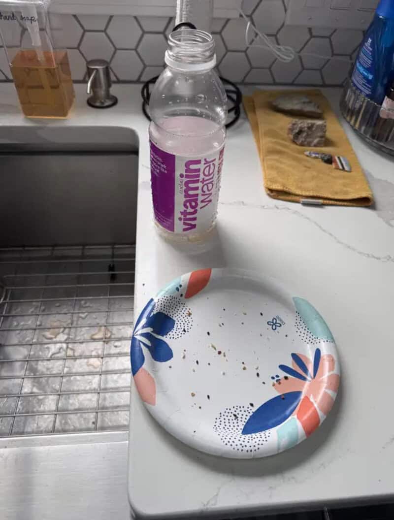 Vitamin water bottle on kitchen counter with plate, towel, and soap nearby.