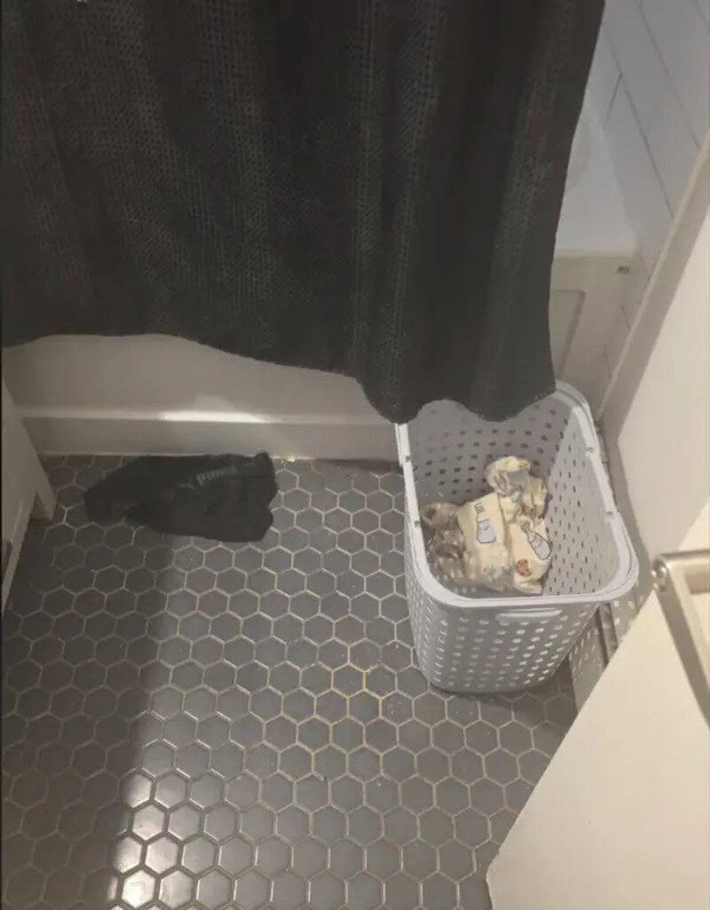 Laundry basket with clothes on a hex tile floor, black curtain, and a black sock.