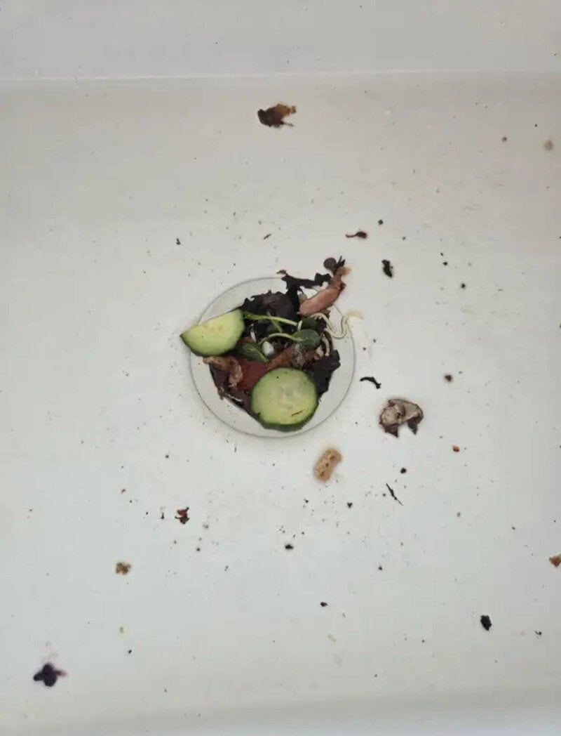 Dirty sink drain with food scraps and debris around it.