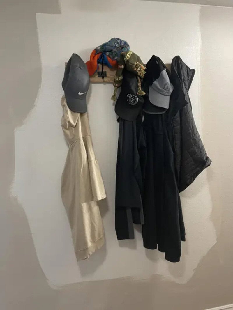 Hats and jackets hanging on a wall hook, with a white wall background.