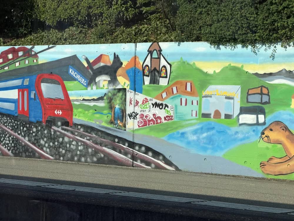 Colorful mural of a train, houses, mountains, and a bear on a wall.