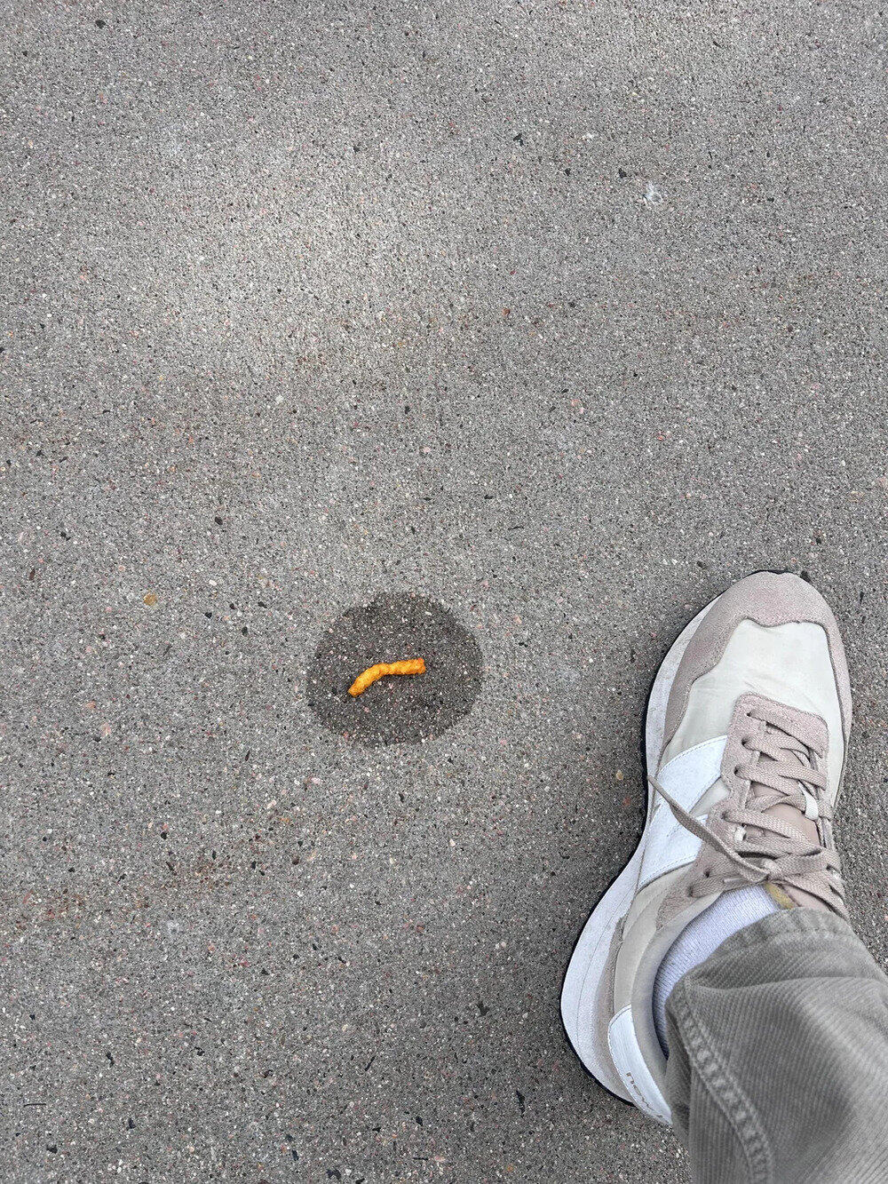 Foot in white sneaker near a small yellow worm on the ground.