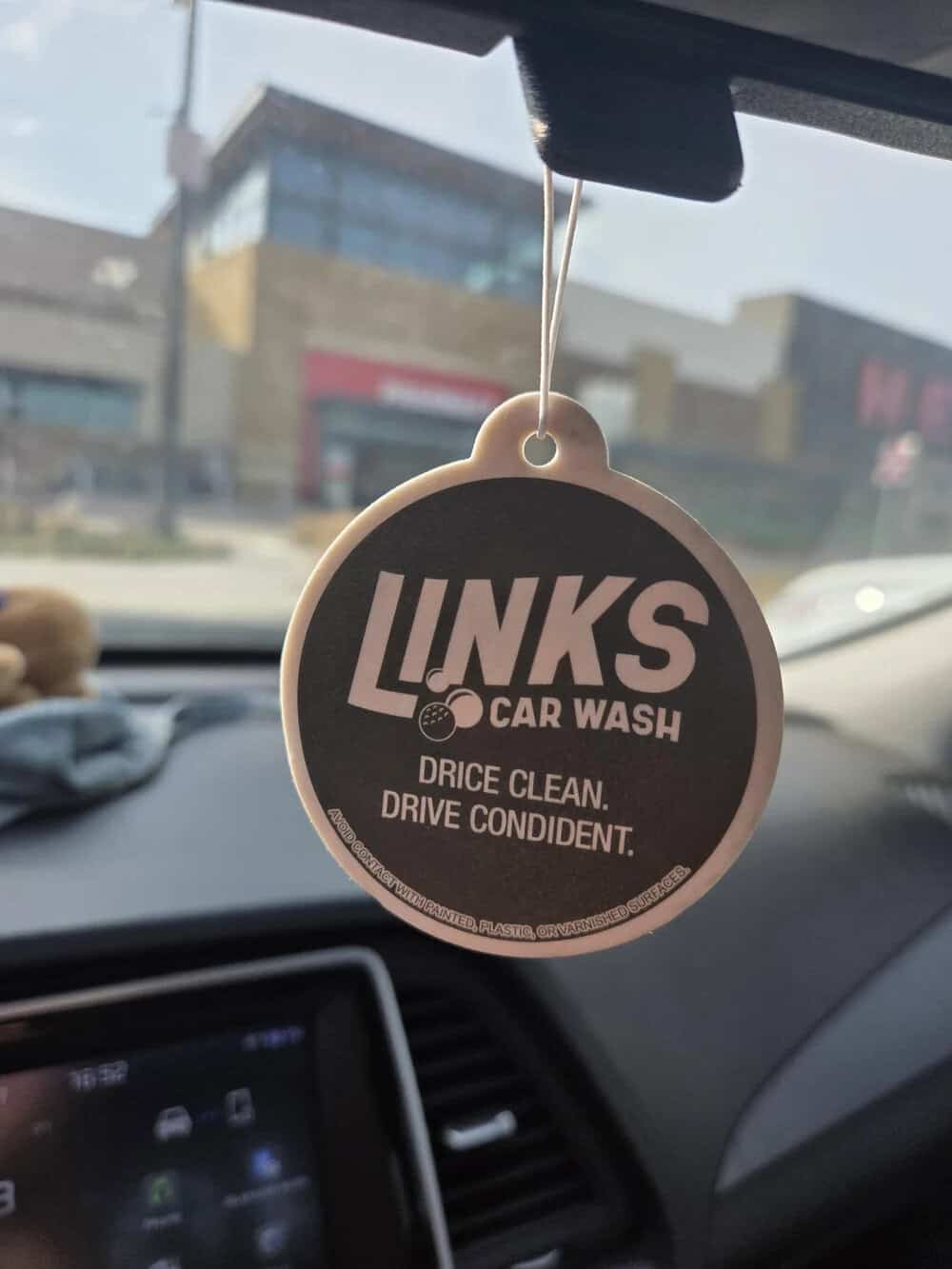LINKS Car Wash air freshener hanging inside a car with buildings outside.