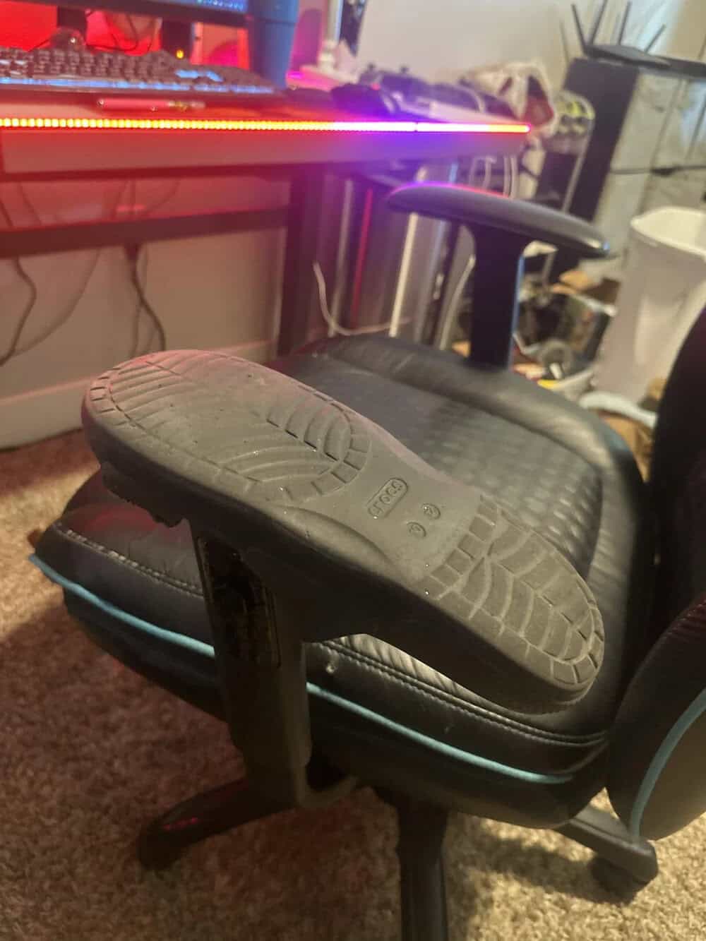 Office chair with a worn-out sole on the footrest in front of a computer desk.