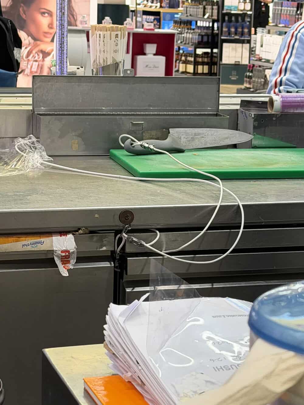 Counter with a green cutting board, a knife, and a pile of papers in a store.