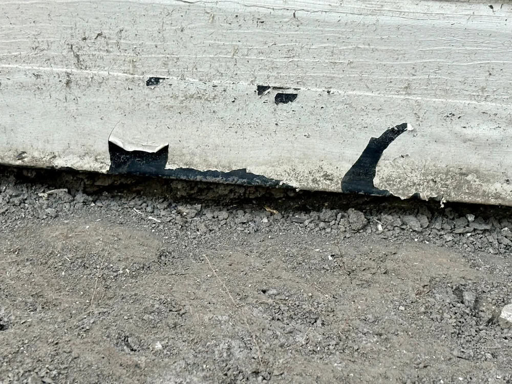 Cracked concrete wall with chipped paint and exposed dirt below.