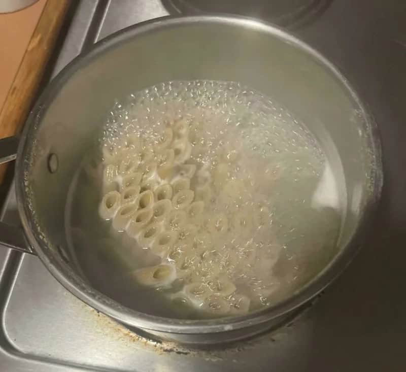 Boiling pasta in a pot on a stove, with bubbles and water.