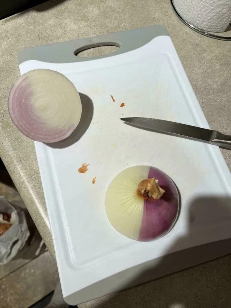 Half onion on a white cutting board with a knife, showing purple and white layers.