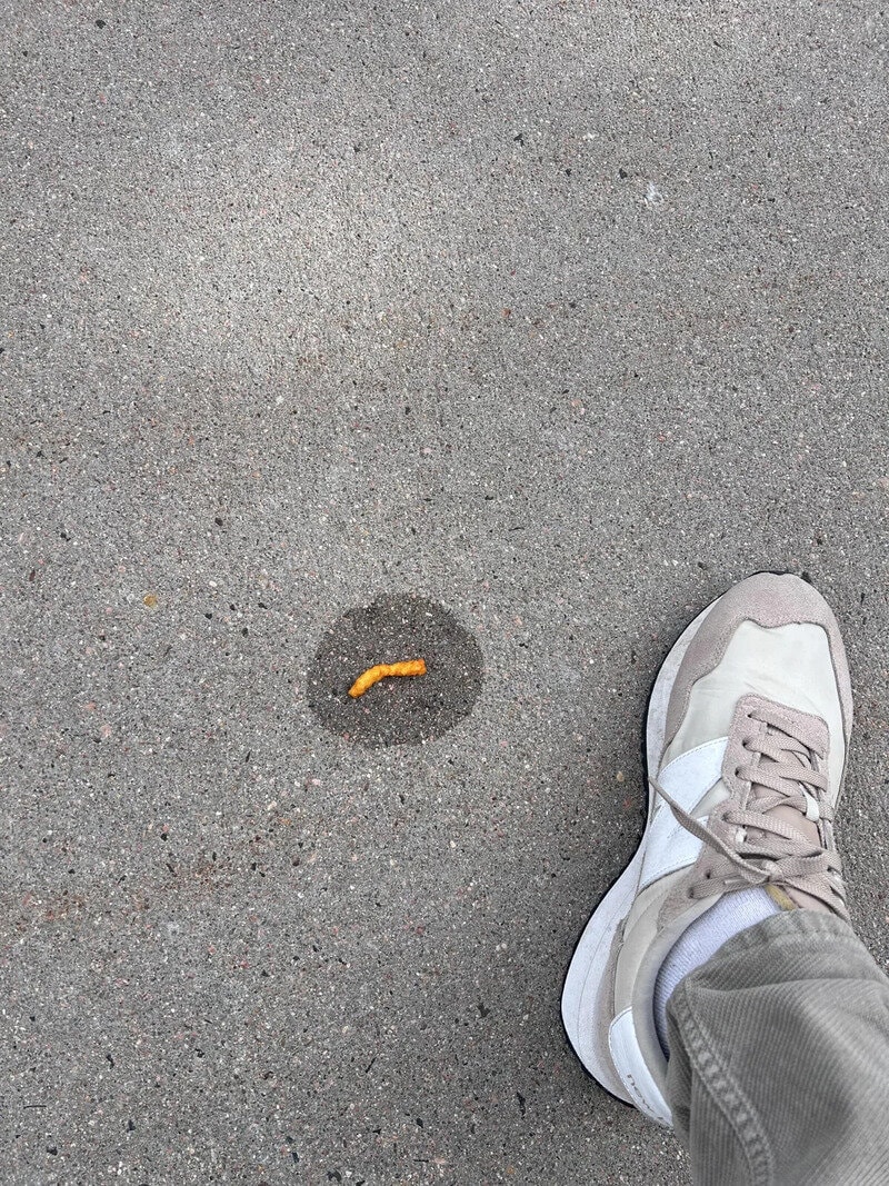 Person's foot in a white sneaker near a small yellow caterpillar on the ground.