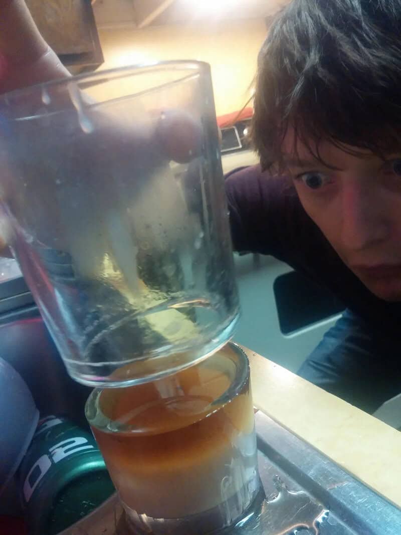 Young man looking at a glass with a layered drink on a table.