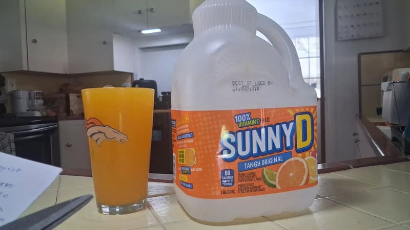 A large Sunny D bottle and a glass of orange juice on a kitchen counter.