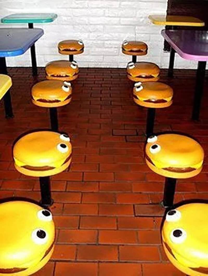 Yellow burger-shaped stools with googly eyes at a fast-food restaurant.