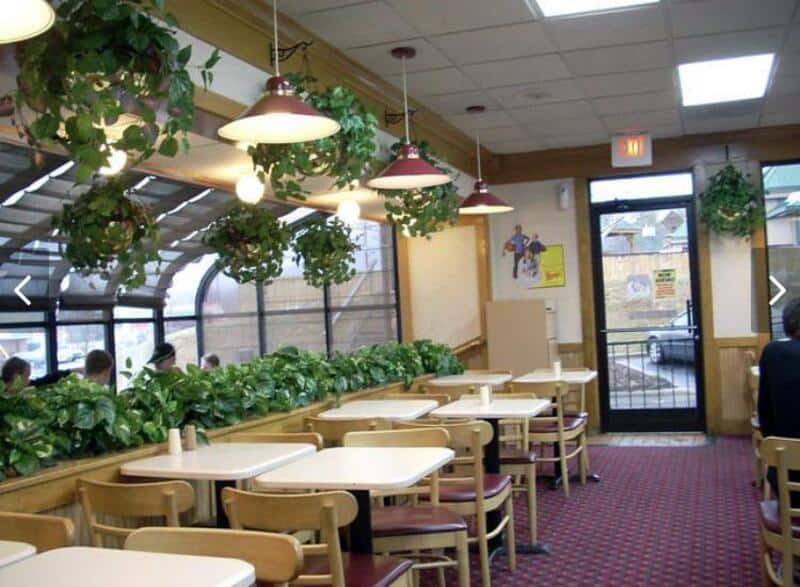Interior of a fast-food restaurant with hanging plants and empty tables.