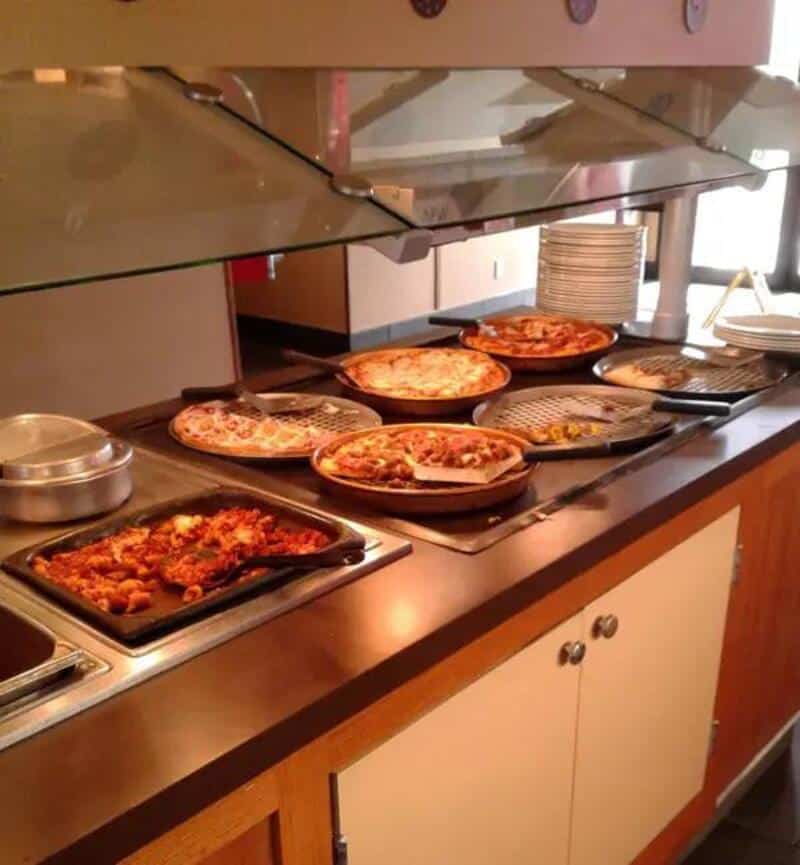 Variety of pizzas on a buffet table at a fast-food restaurant from the 80s or 90s.