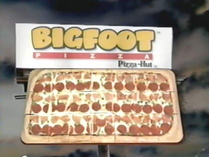 Large pepperoni pizza from Pizza Hut with a Bigfoot Pizza Hut sign in the background.