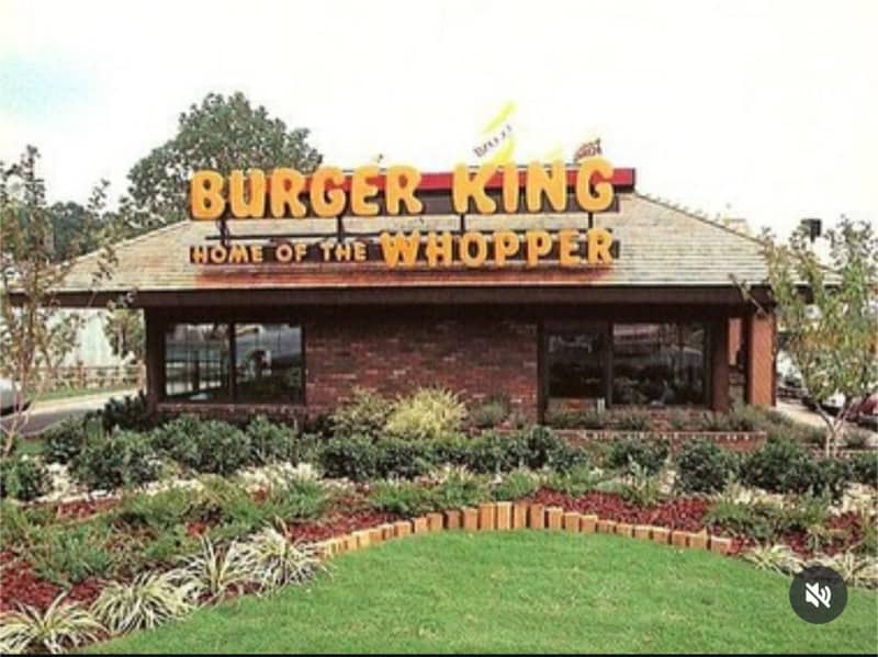 Burger King restaurant with sign 'Home of the Whopper' in front of a garden.