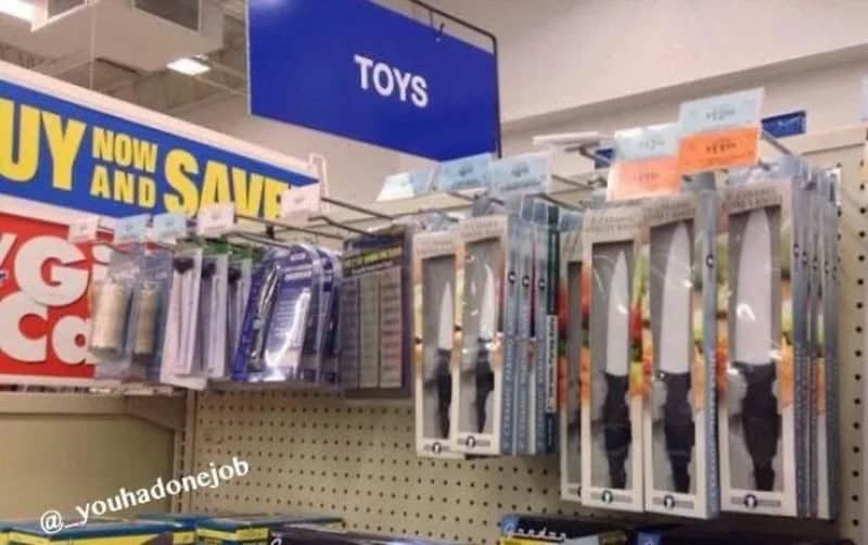 Toy knives hanging on a store shelf under a 'TOYS' sign.