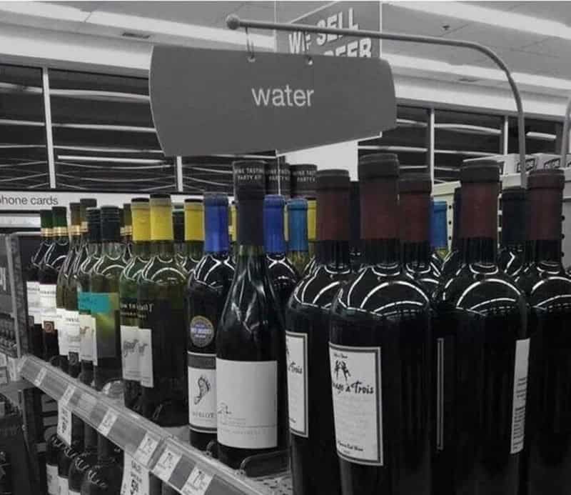 Bottles of water on a store shelf with a sign labeled 'water' above them.