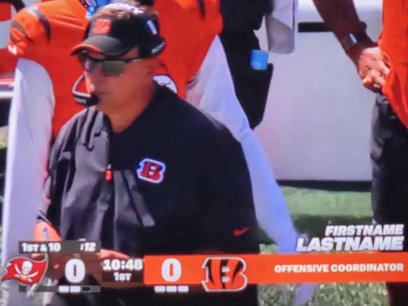 Offensive coordinator wearing black cap and jacket with Bengals logo during game.