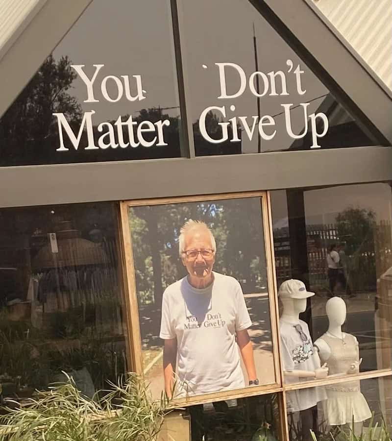 A man with glasses and a white t-shirt that says 'Don't Matter, Don't Give Up' standing in front of.