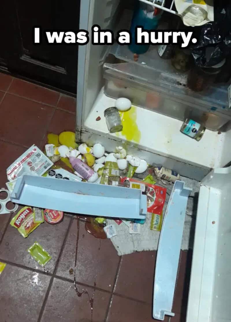 Open refrigerator with spilled eggs and food on the floor.