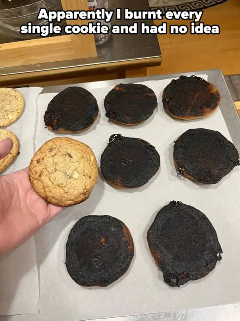 Burnt cookies on a baking sheet with one normal cookie in hand.