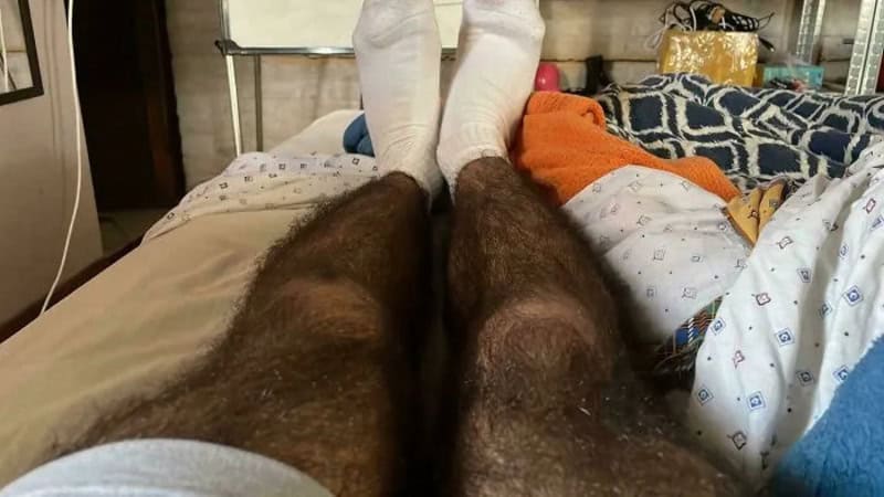 Close-up of hairy legs with white socks on a bed.