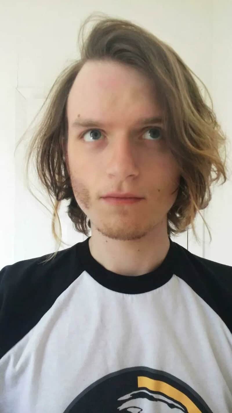 Young man with long, wavy hair and blue eyes, wearing a black and white shirt.
