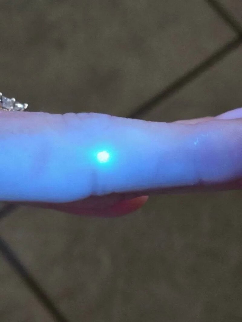 Fingertip glowing with a blue light in a dark environment.