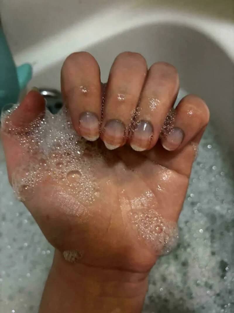 Fist with short, uneven nails in soapy water.