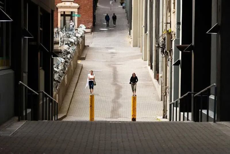 Two women walking on a city street with buildings on both sides.