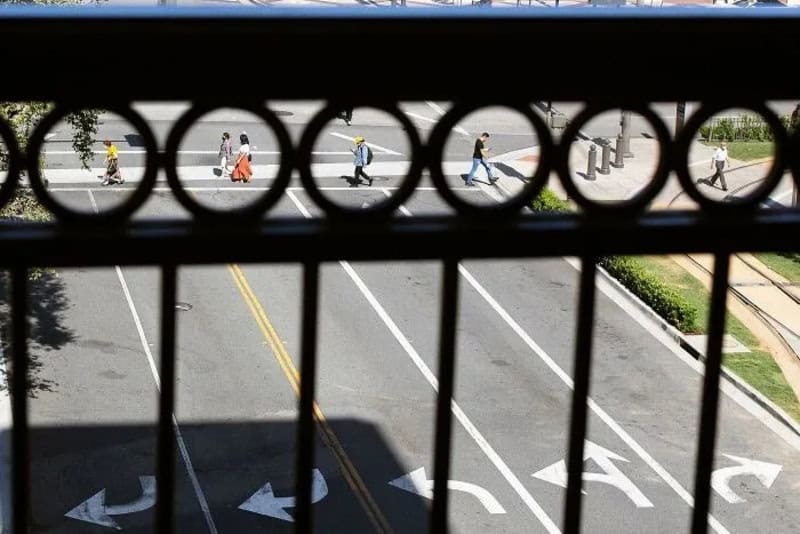 Pedestrians crossing street seen through a circular-patterned fence.