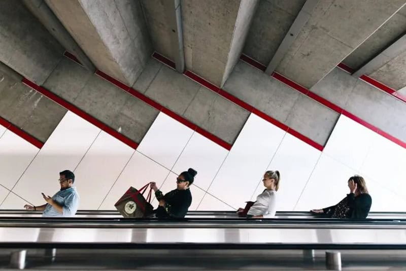 Four people standing on an escalator in a modern building with concrete ceiling.