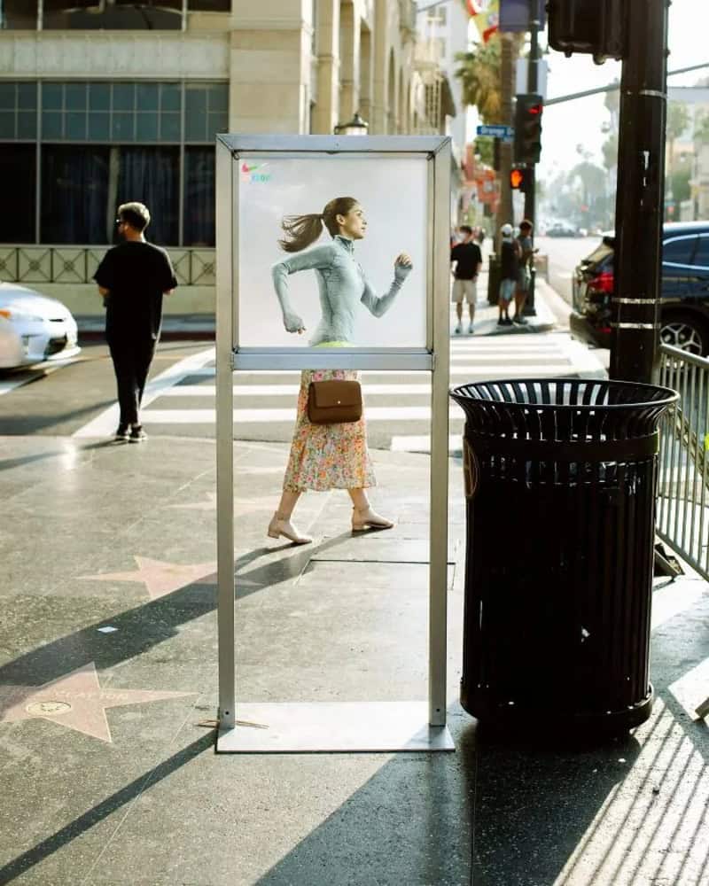 Woman walking past a bus stop with a large advertisement in Los Angeles.