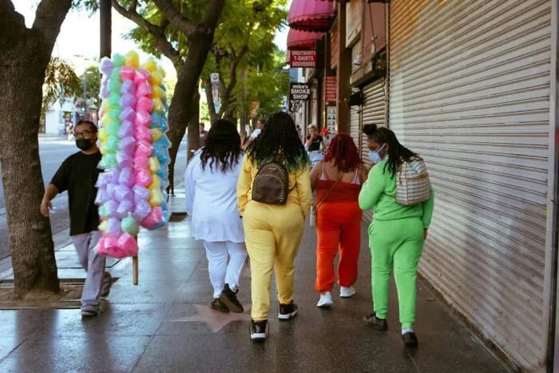Group of diverse women walking on a city sidewalk with colorful balloons and closed shops.