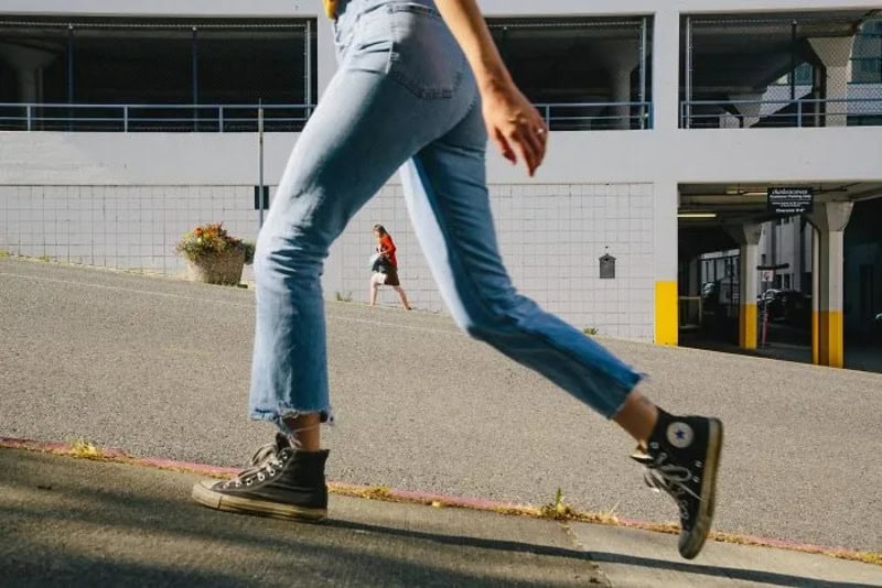 Close-up of a person walking in jeans and sneakers on a city street.