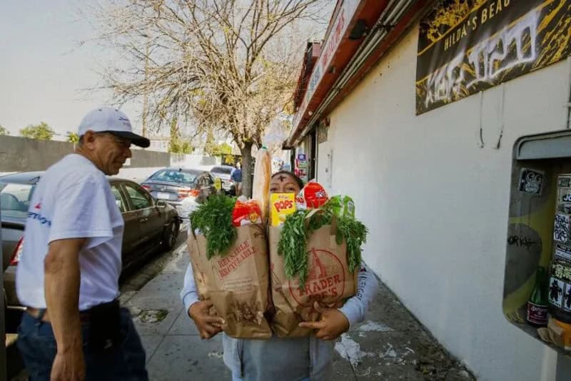 Person with a large bag of groceries on a city sidewalk, another person nearby.