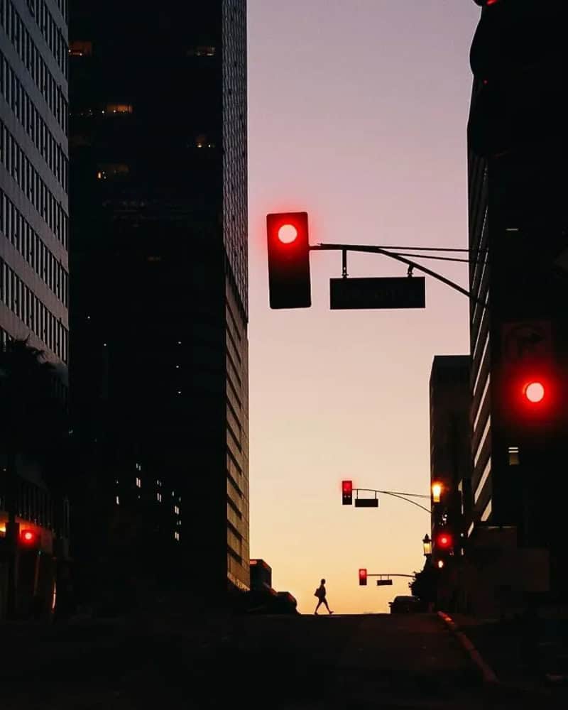 Silhouette of a person crossing a city street at sunset with traffic lights.