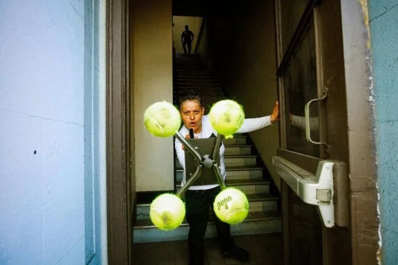 Woman holding tennis balls in a doorway with a man on stairs in background.